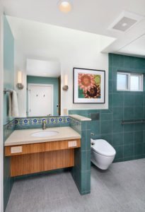 A universal design bathroom inspired by Catalina tiles features a wall-mounted toilet and a roll-under vanity.