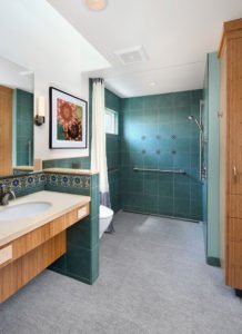 A universal design bathroom inspired by Catalina tiles features a curbless shower with hand railings, a wall-mounted toilet, and a roll-under vanity.