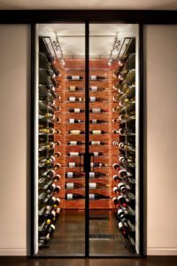 A modern wine cellar is illuminated from the back and showcased through glass doors