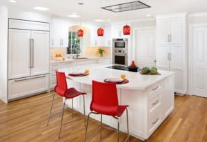 A light-filled kitchen adds pops of red against an otherwise white color palette.