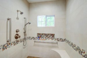 A roll-in shower features two shower heads, multiple hand railings, and a bench.