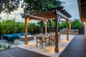 A pergola covers an outdoor dining area near a firepit and lounge seating.