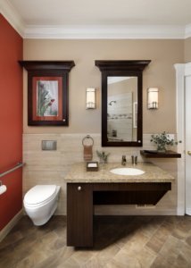 A universal design bathroom has a wall-mounted toilet with a flush plate and roll-under vanity.