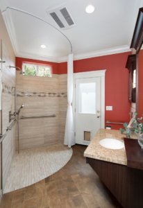 A universal design bathroom features a corner curbless shower with two shower heads, hand rails, and a roll-under vanity.