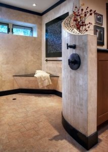 A universal design bathroom has a large, open curbless shower with a bench and brushed handrail in the corner.