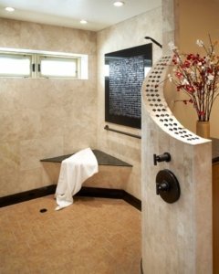 A natural, universal design bathroom features a large, open curbless shower with a bench and brushed handrail in the corner.