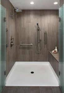 A universal design bathroom has a roll-in shower with brushed silver railings, dual shower heads, and a bench.