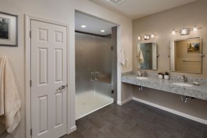 A contemporary universal design bathroom features a curbless shower with closed, frosted glass doors and a roll-under vanity with two sinks.