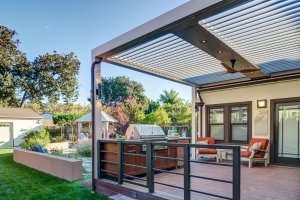 A metal pergola with movable louvers covers an outdoor kitchen and grill.
