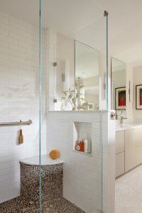 This shower's pony wall provides a storage nook next to a stone-accented corner seat.